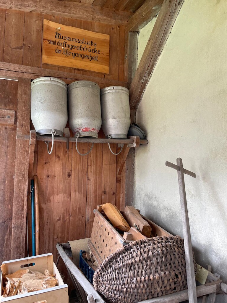 Alte Milchkannen, Holzwagen und Körbe erinnern an den bäuerlichen Alltag vergangener Zeiten. Ein Schild mahnt: 