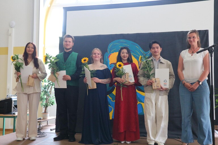 Auf der Bühne stehen fünf Absolventinnen und Absolventen mit ihrer Klassenlehrerin.