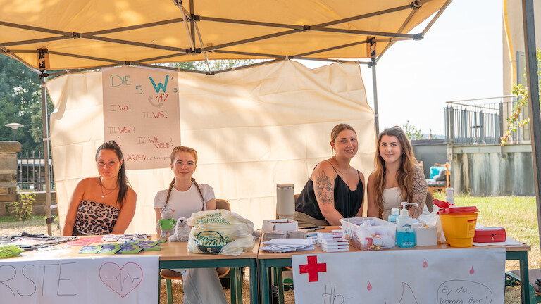 Vier MFA-Schülerinnen sitzen an ihrem Stand.