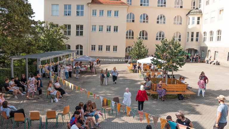 Schülerinnen und Schüler suchen schattige Plätze auf dem Schulinnenhof.