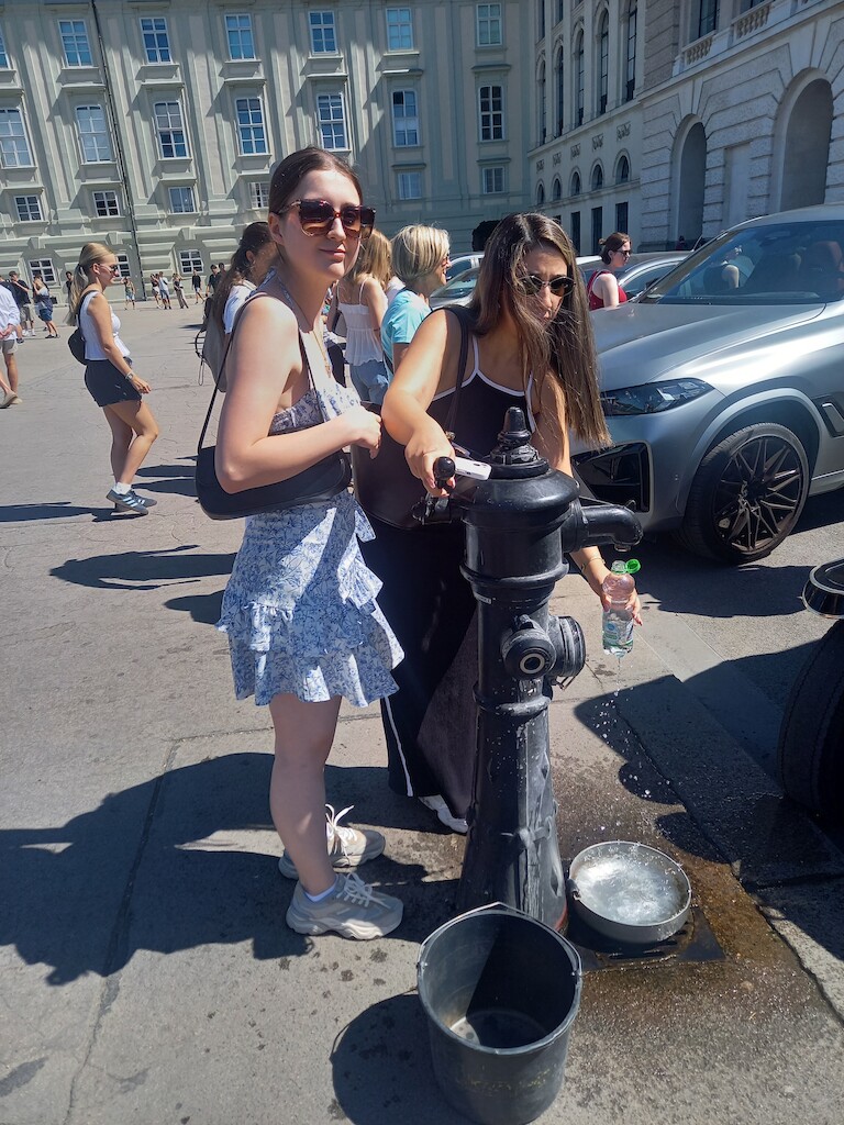 Zwei Schülerinnen füllen ihre Flaschen an einer Trinkwassersäule.