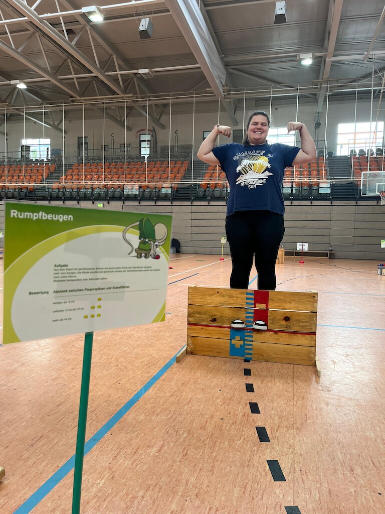 Eine Schülerin posiert neben dem Schild Rumpfbeugen.