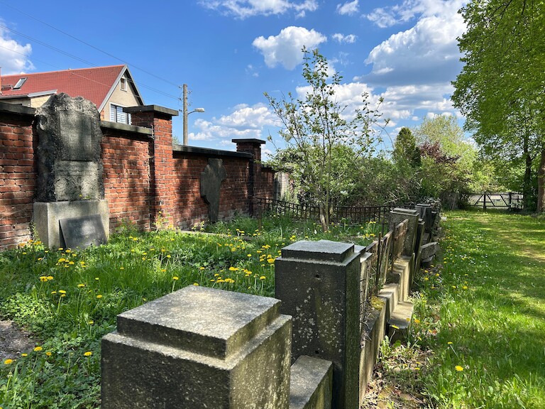 Das Denkmal von der Seite. Davor eine Mauer im Friedhof.