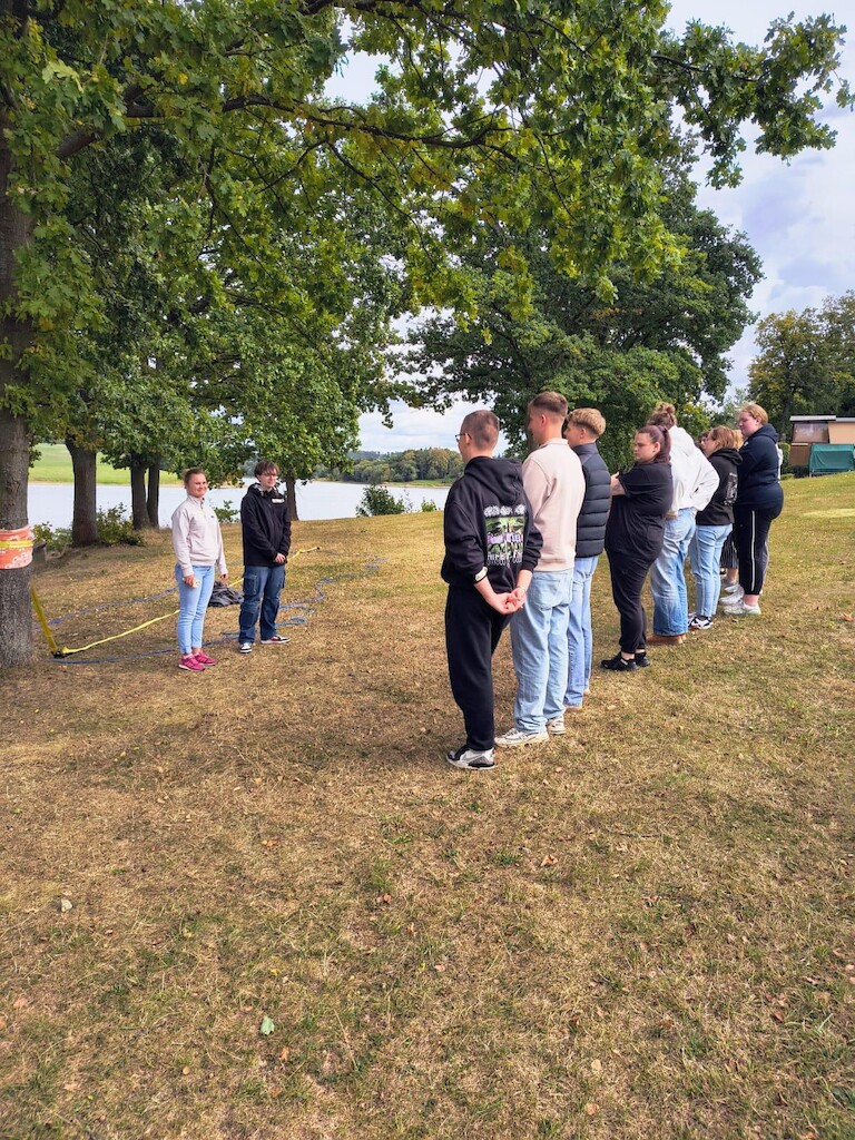 Die Schülerinnen und Schüler stehen in einer Reihe und hören die Anweisungen zwei anderer Schüler.
