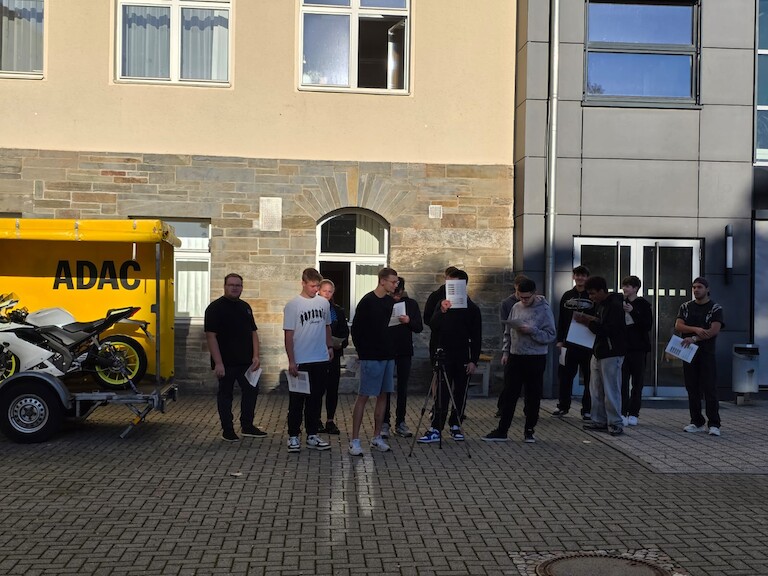 Die Schüler stehen mit ihrem Blättern in einer Reihe und hören zu.