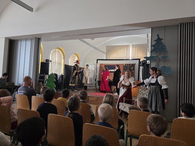 Schülerinnen und Schüler stehen auf der Bühne. Das Publikum ist von hinten zu sehen.