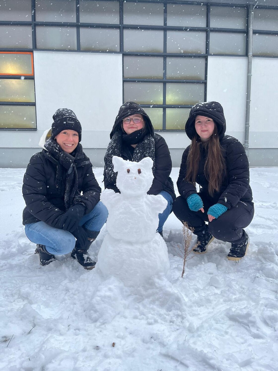 Drei Schülerinnen posieren hinter ihrer gebauten Schneefigur.