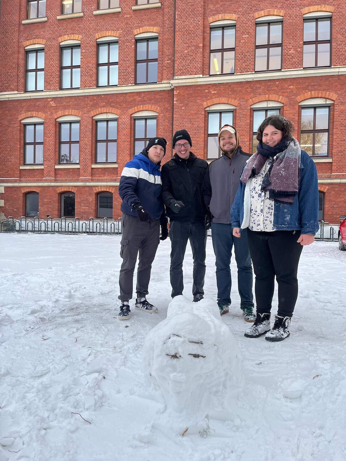 Vier Schülerinnen und Schüler posieren hinter ihrer gebauten Schneefigur.