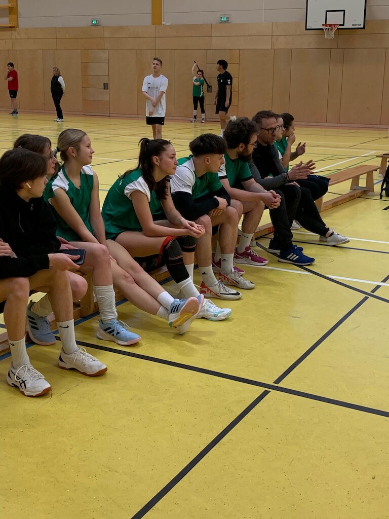 Die Zuschauer am Spielfeldrand auf einer Bank.