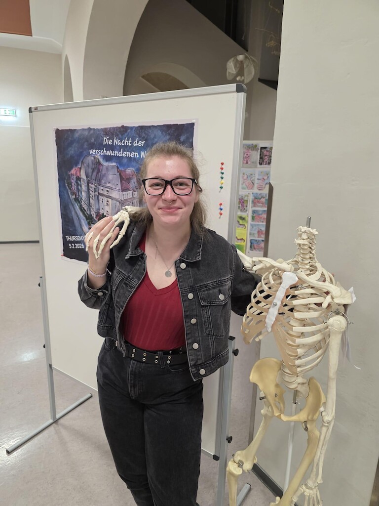 Schüler mit Skelett vor dem Plakat.