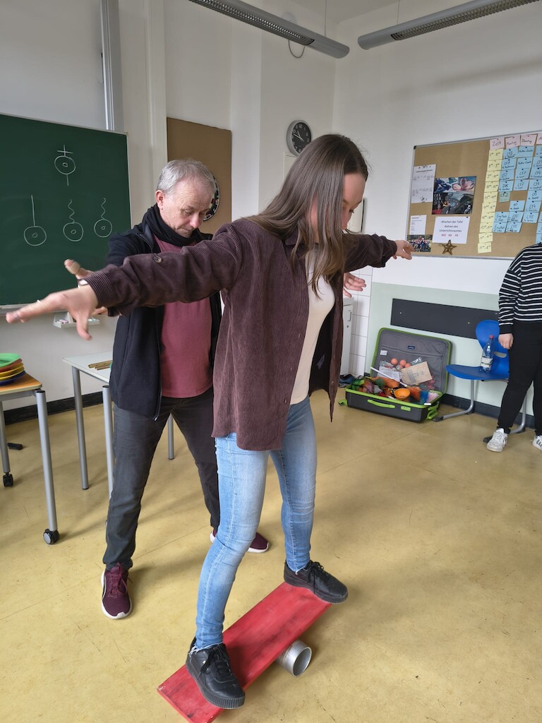 Eine Schüler balanciert auf einem Brett, das auf einer Rolle liegt.