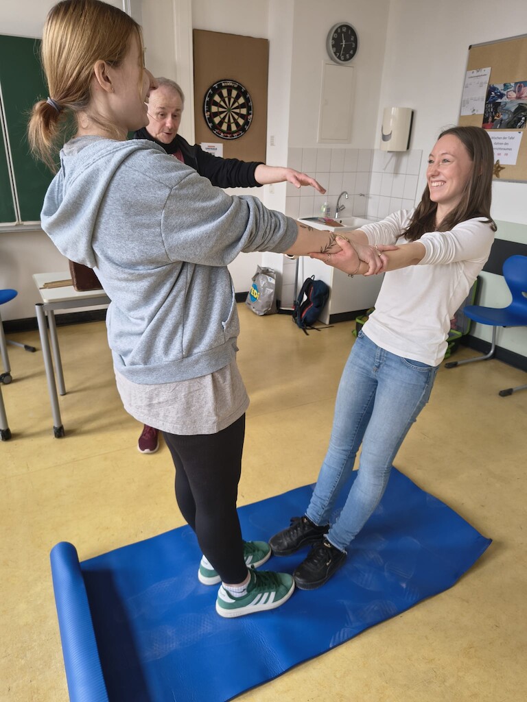 Zwei Schülerinnen stehen sich gegenüber, halten sich an den Händen fest und lassen sich zurückfallen.