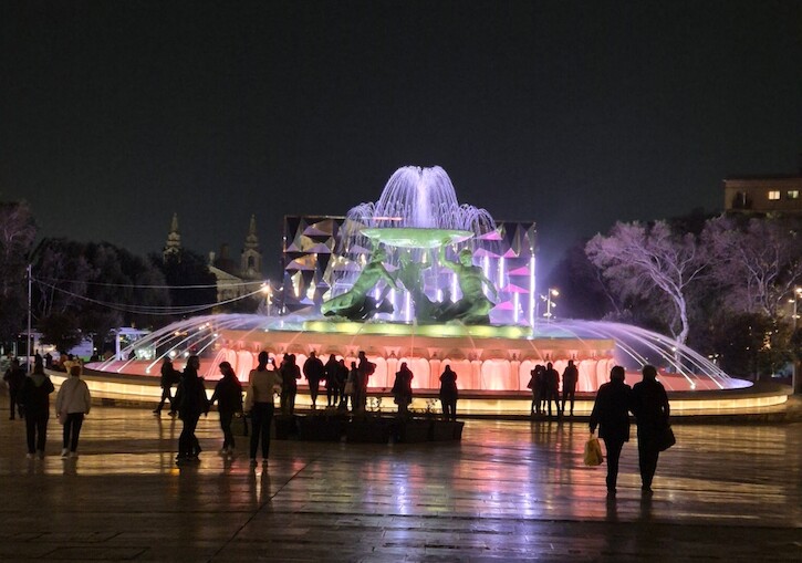 Eine butn beleuchteter Brunnen in der Nacht.