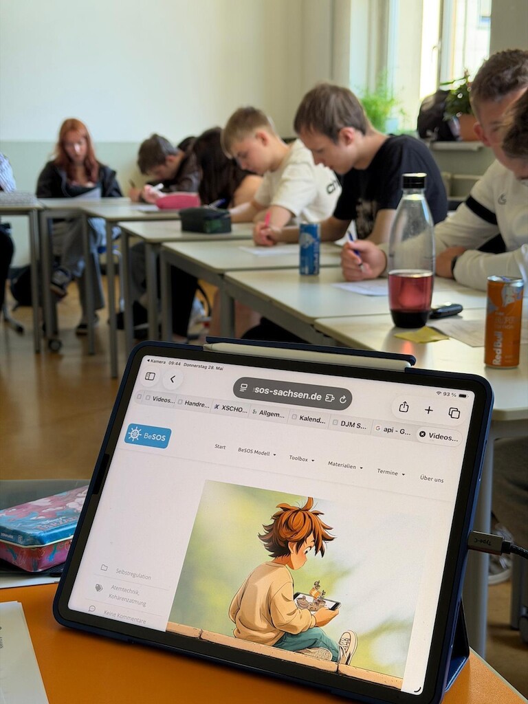 Die Schüler im Klassenraum. Es ist ein Tablet mit der Seite SOS Sachsen zu sehen